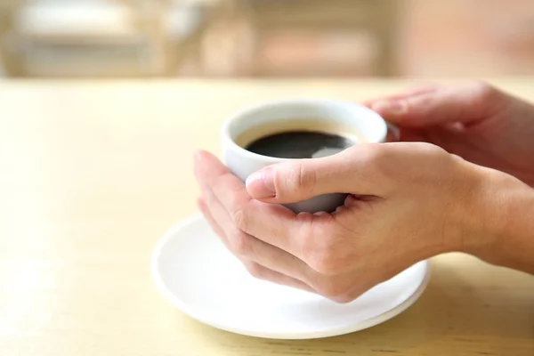Secangkir kopi dengan tangan di atas meja di latar belakang kafe — Stok Foto