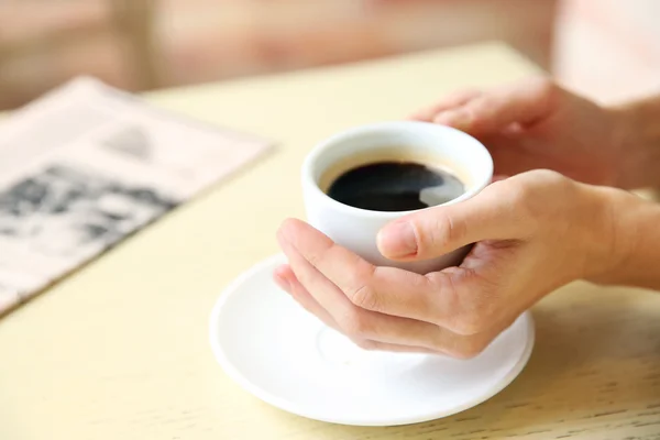 Secangkir kopi dengan tangan dan koran di atas meja dengan latar belakang kafe — Stok Foto