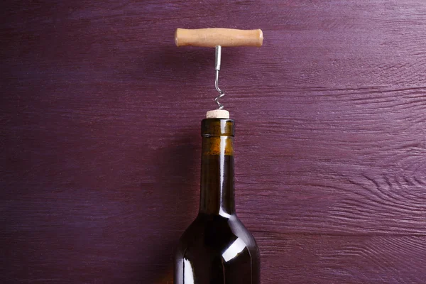 Corkscrew and wine bottle on purple wooden background — Stock Photo, Image