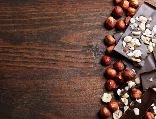 Pedaços de chocolate com nozes em fundo de madeira — Fotografia de Stock