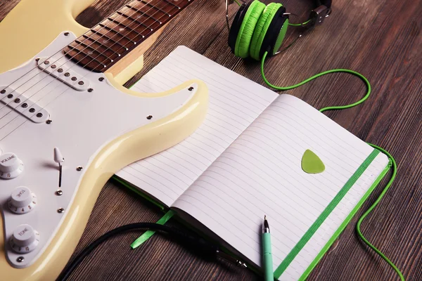 Elektrická kytara s zelená sluchátka a Poznámka: kniha o dřevěné pozadí — Stock fotografie