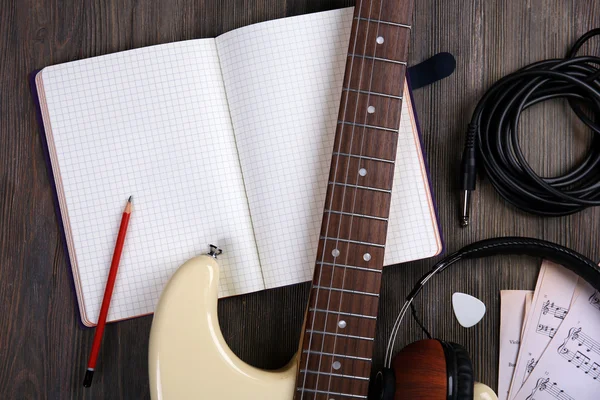 Electric guitar with headphones, musical notes and note book on wooden background — Stock Photo, Image