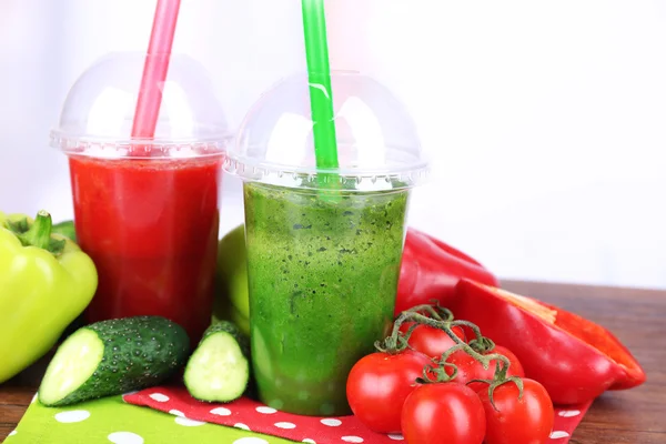 Свежие овощные соки в пластиковых чашках на деревянном столе, на светлом фоне — стоковое фото