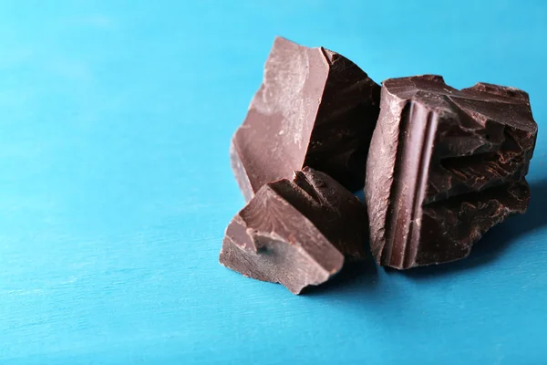 Mörk choklad bitar på färg trä bakgrund — Stockfoto