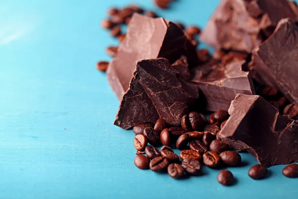 Black chocolate pieces and coffee grains on color wooden background — Stock Photo, Image