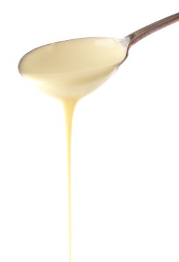 Condensed milk pouring from a spoon, isolated on white clipart