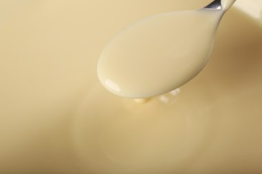 Background of condensed milk and a spoon in a bowl, close-up clipart