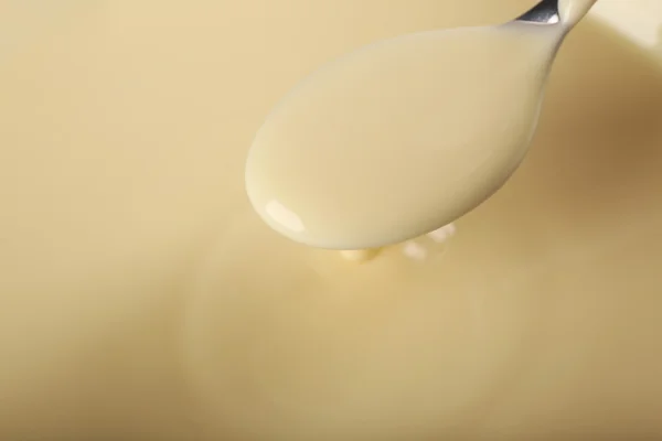 Background of condensed milk and a spoon in a bowl, close-up — Stock Photo, Image