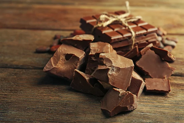 Chocolate pieces, shavings and cocoa beans on color wooden background — Stock Photo, Image