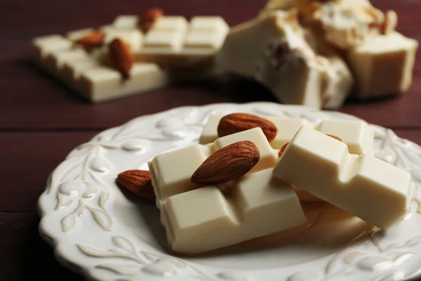 Части белого шоколада с орехами на тарелке, на фоне цвета дерева — стоковое фото