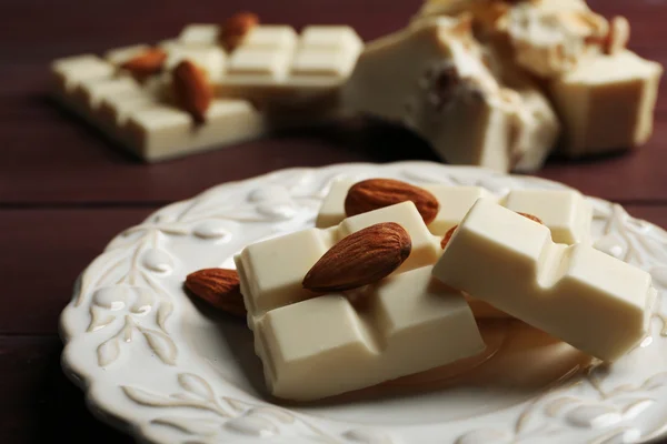 White chocolate pieces with nuts on plate, on color wooden background — Stock Photo, Image