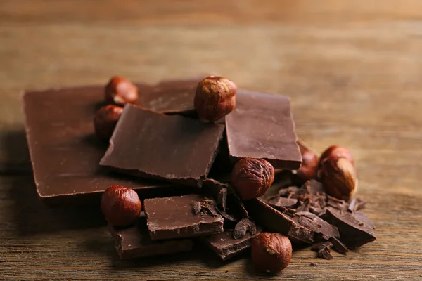 Pedaços de chocolate preto com nozes no fundo de madeira — Fotografia de Stock