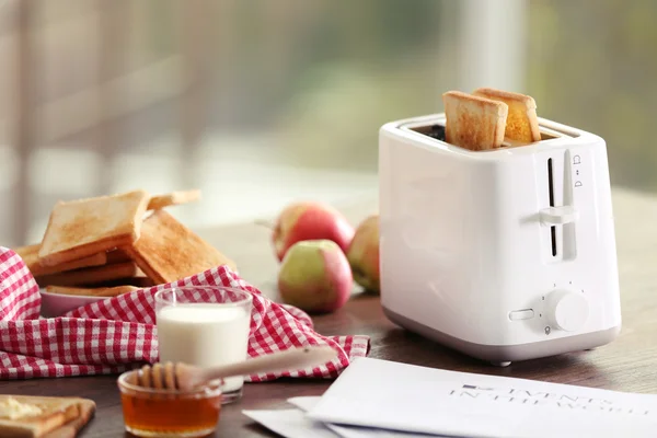 Mesa servida para café da manhã com torradas, leite e mel, em fundo embaçado — Fotografia de Stock
