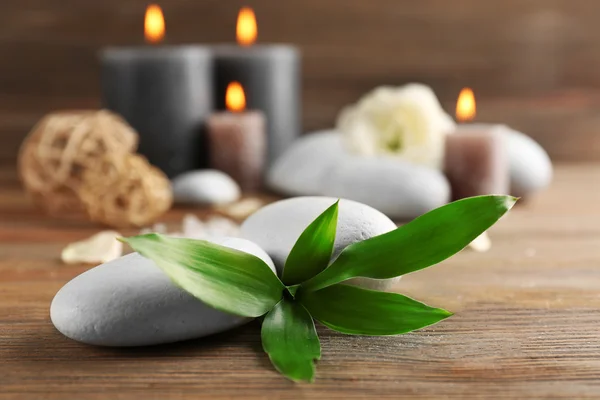 Relax set contains alight wax candles with flowers and pebbles on wooden background, focus on green leaf — Stock Photo, Image