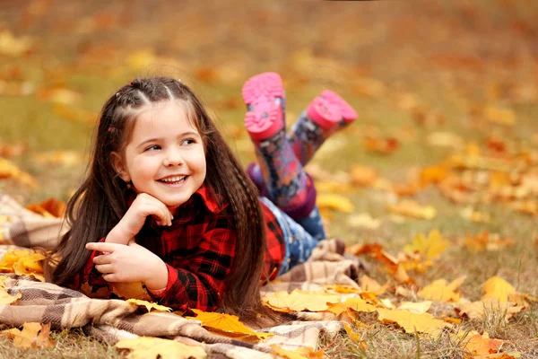 Gelukkig jong meisje liggend op plaid in herfst park — Stockfoto