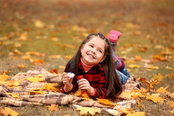 Leuk meisje liggend op plaid en blazen van zeepbellen in park — Stockfoto