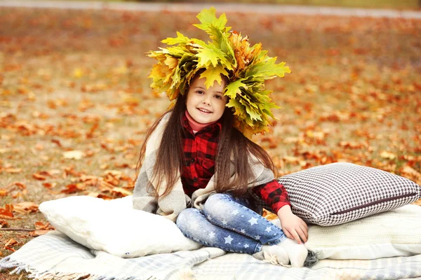 Gelukkig jong meisje in gele herfst krans zittend op plaid in park — Stockfoto
