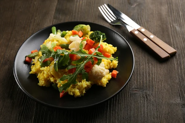 Svart plåt med vegetabiliska risotto, gaffel och kniv på träbord — Stockfoto