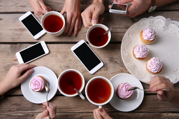 Quatre mains avec téléphones intelligents tenant tasses avec thé, sur fond de table en bois — Photo