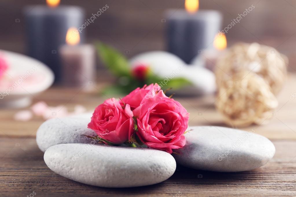 Alight wax grey candles with roses and pebbles on wooden background