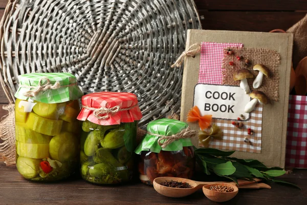 Pots avec légumes marinés, haricots, épices et ustensiles de cuisine sur fond en bois — Photo