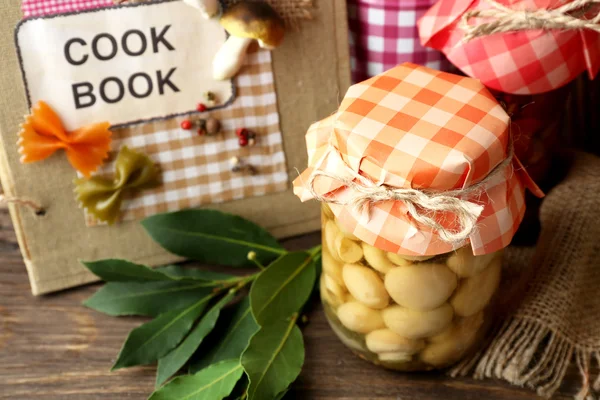 Gläser mit eingelegtem Gemüse, Bohnen, Gewürzen und Geschirr auf hölzernem Hintergrund — Stockfoto