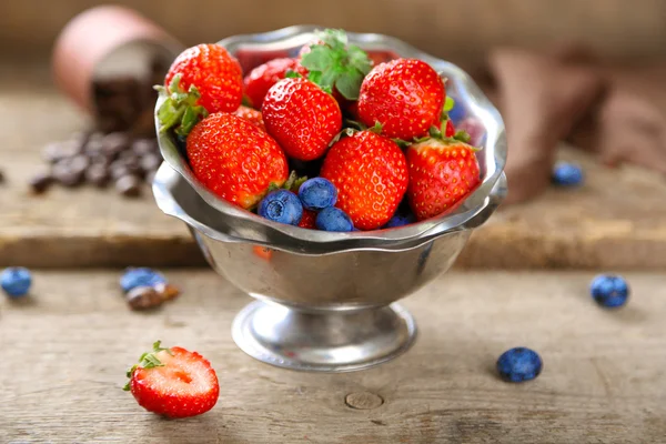 Ripe sweet different berries in bowl, on old wooden table — Stock Photo, Image