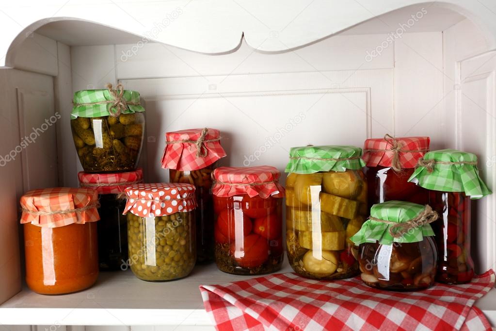 Jars with pickled vegetables and beans on wooden shelf