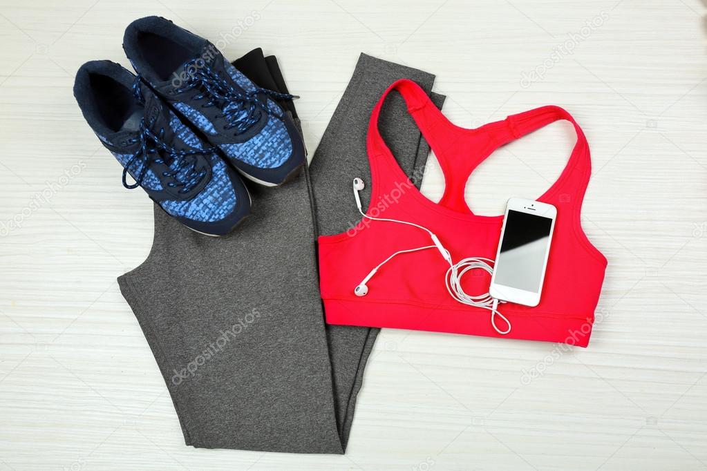 Sport clothes, shoes  and smart phone with earphones on light background