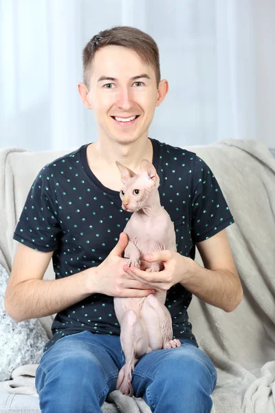 Mladý pohledný muž držící kočku na gauči doma — Stock fotografie
