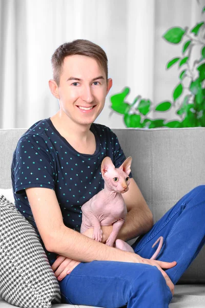 Junger schöner Mann sitzt mit Katze auf Couch zu Hause — Stockfoto