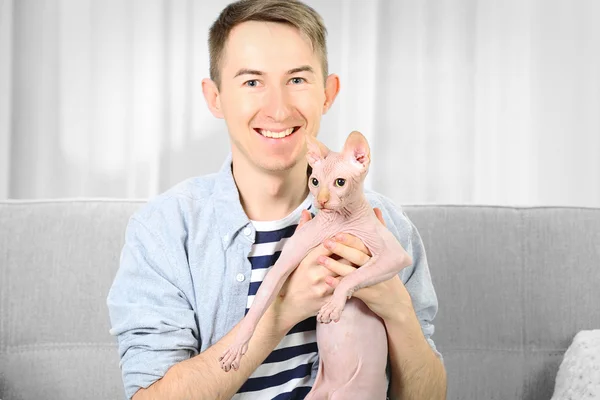 Νέος όμορφος άνθρωπος που κρατά μια γάτα στον καναπέ στο σπίτι — Φωτογραφία Αρχείου