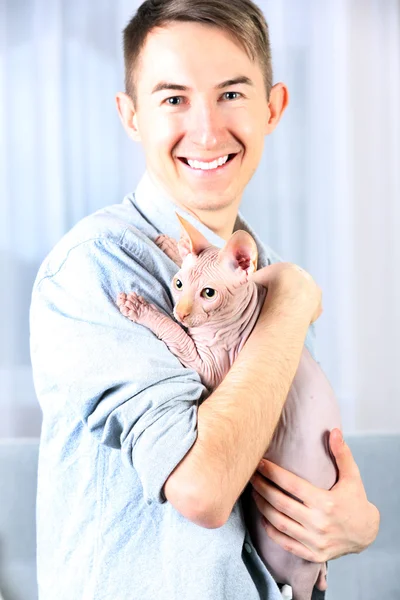 Young handsome man holding a cat on light tulle background — Stock Photo, Image