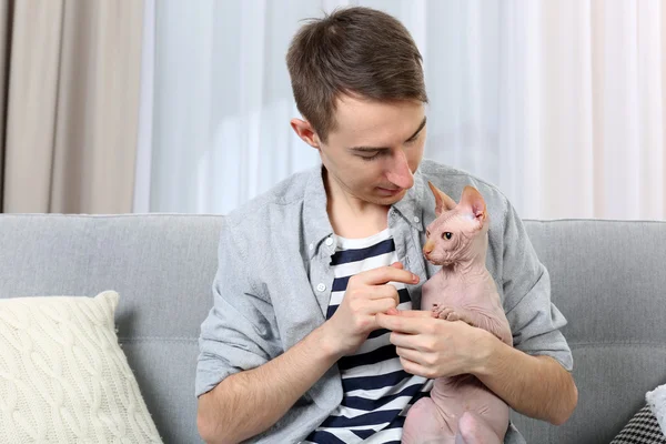 Mladý pohledný muž držící kočku na pozadí světlé místnosti — Stock fotografie