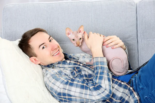 Junger schöner Mann liegt mit Katze auf Couch zu Hause — Stockfoto