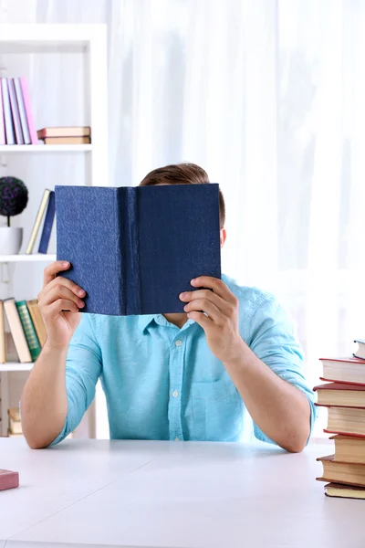 Junger Mann liest Buch am Tisch — Stockfoto