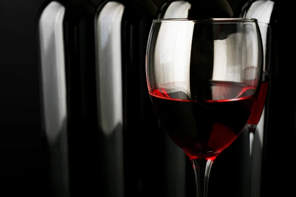 Red wine glass against bottles — Stock Photo, Image