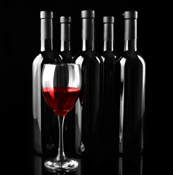 Red wine glass against bottles — Stock Photo, Image