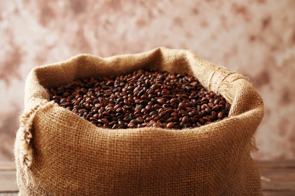 Saco con granos de café tostados sobre fondo marrón claro — Foto de Stock
