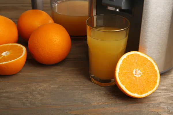 Stainless juice extractor with glass of orange juice on wooden background, close up — Stock Photo, Image