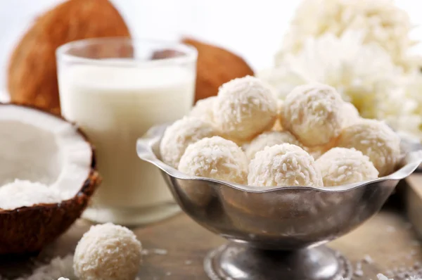 Homemade sweets in coconut flakes and fresh coconut on tray, close-up