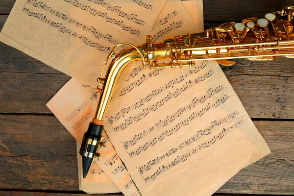 Saxofone dourado bonito com notas musicais em fundo de madeira, close-up — Fotografia de Stock