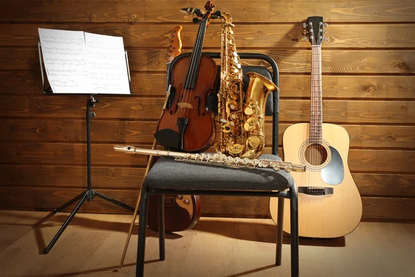 Musical instruments on a chair and note holder against wooden background — Stock Photo, Image
