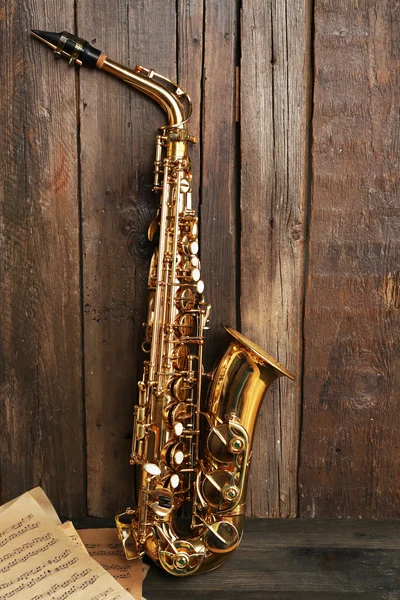 Saxofone dourado bonito com notas musicais em fundo de madeira, close-up — Fotografia de Stock