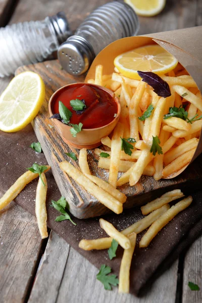 French fried potatoes in craft paper on cutting board — Stock Photo, Image