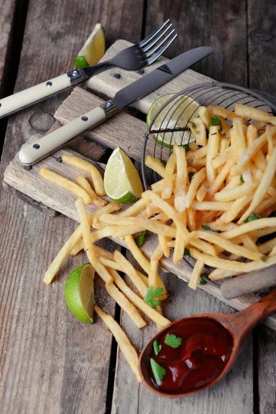 French fried potatoes in metal basket with sauce and lime on cutting board — Stock Photo, Image