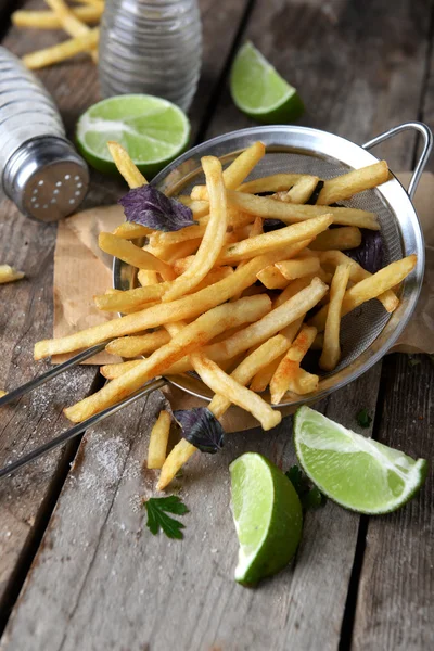 French fried potatoes in metal colander with sauce on wooden background — Stock Photo, Image