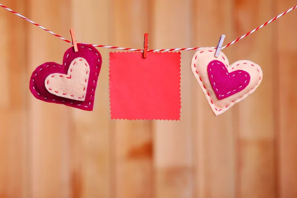 Текстильные сердца и пустой лист висят на веревке на деревянном фоне — стоковое фото