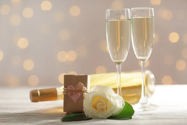 Bicchieri di vino, una bottiglia, una rosa bianca e un regalo nella scatola, su sfondo sfocato — Foto Stock