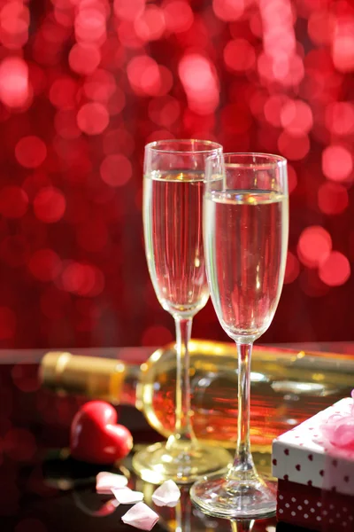 Impostazione di bicchieri con vino, bottiglia e un regalo nella scatola, su sfondo rosso sfocato — Foto Stock